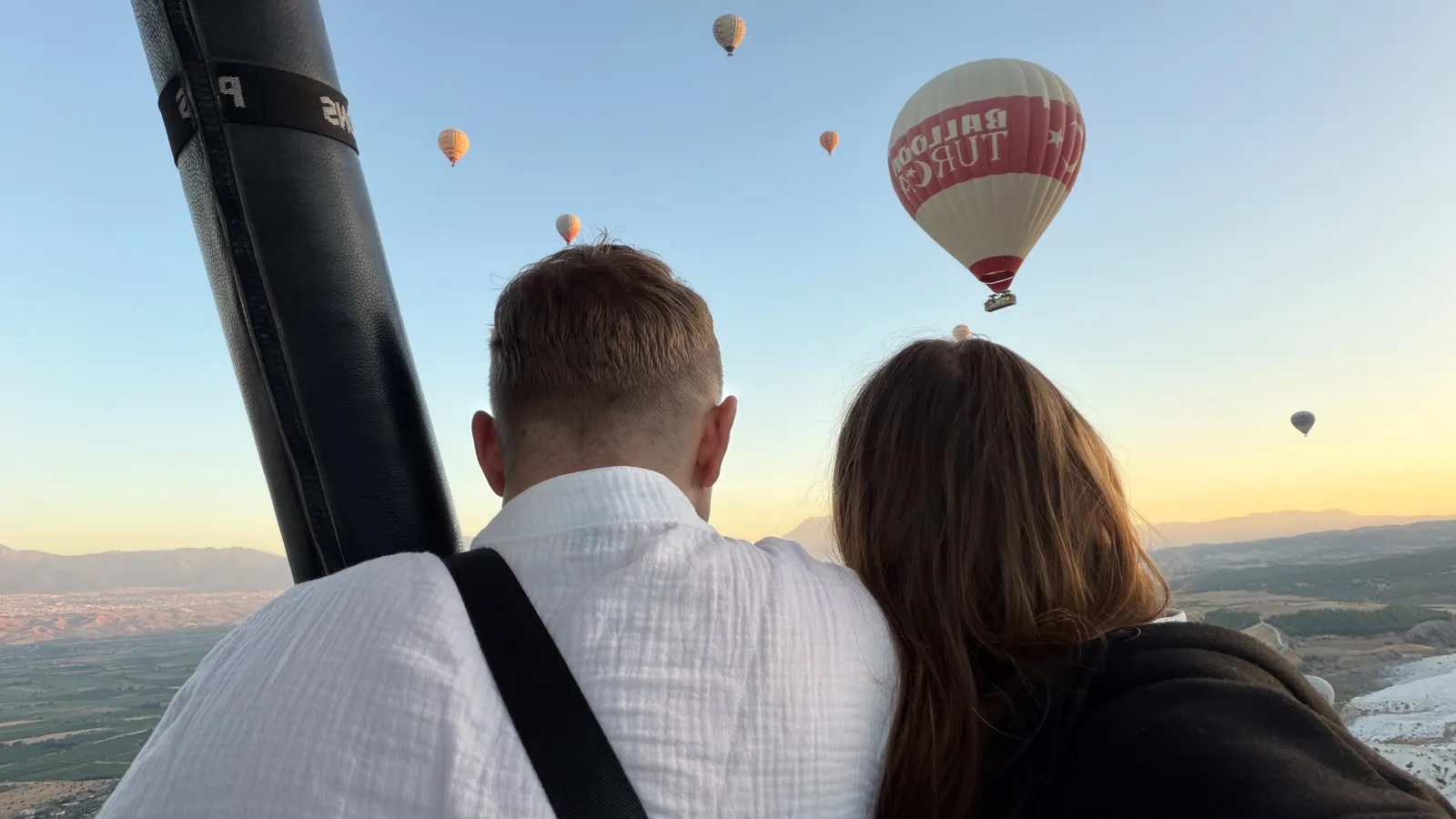 A couple watching hot air balloons at sunrise from a balloon basket