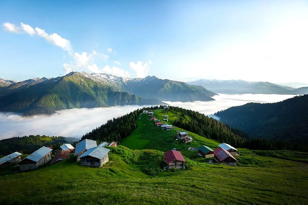 Wooden highland houses on a green ridge above a sea of clouds